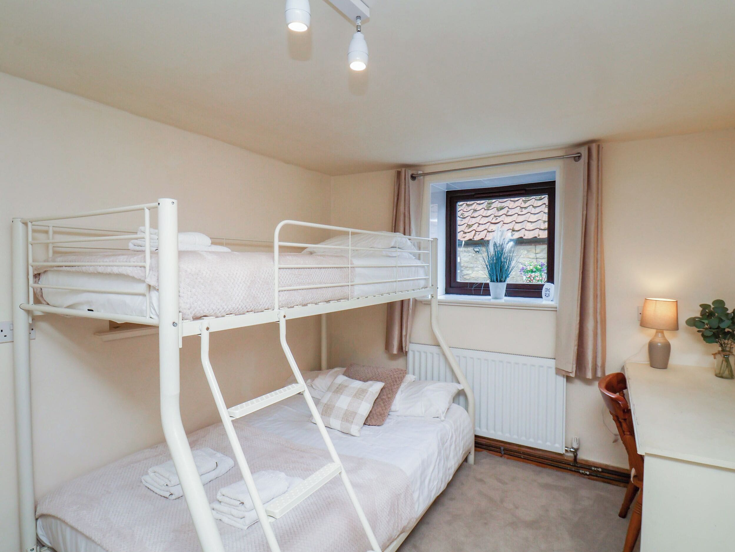 Quarto com beliche, janela, radiador, escrivaninha, cadeira e luminária.