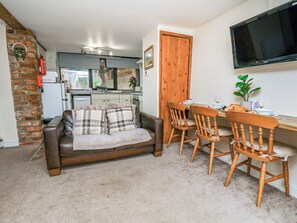 A cozy living room with a brown leather sofa, wooden dining chairs, a flat-screen TV, and a kitchen in the background. - Owl (Pickering)