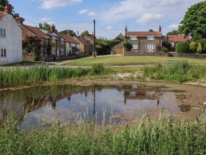 A rural setting with traditional stone houses, a small pond, and surrounding greenery. - Owl (Pickering)
