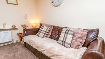 A cozy living room with a brown leather sofa, a white radiator, a wall clock, and a framed picture on the wall.
