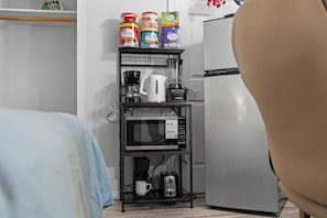 Una cuineta amb microones, cafetera i torradora sobre una prestatgeria, i un frigorífic a la dreta.