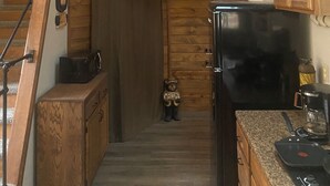 Een cabin interieur met een houten trap, een zwarte koelkast, een magnetron en een decoratieve beer als welkomstcadeau.