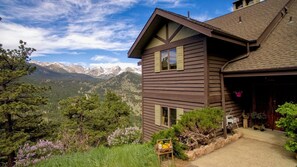 Une maison à deux étages avec vue sur la montagne, un porche à l’avant orné de plantes et un garage.