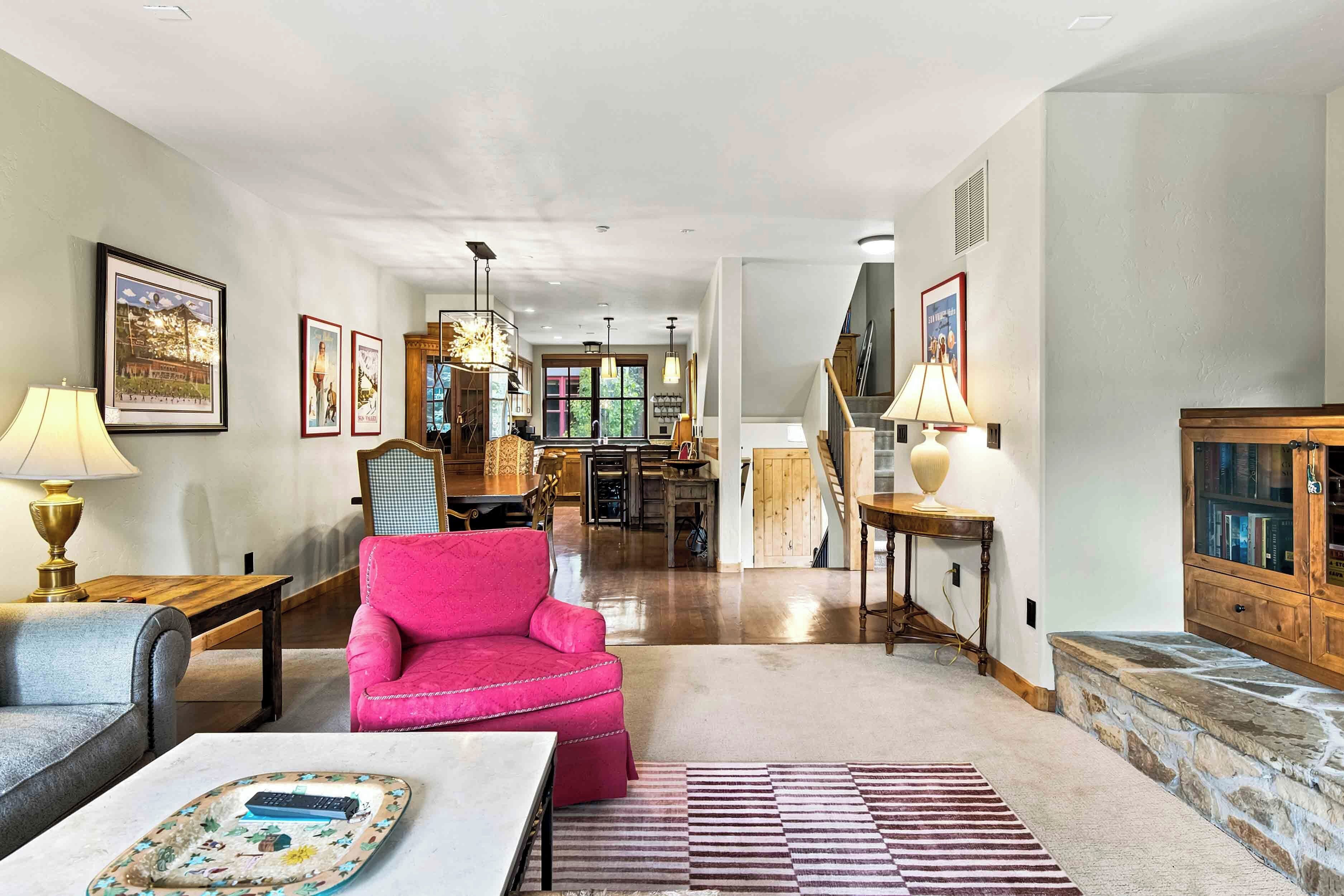 A spacious living room with a bright ceiling, a wooden dining table, a pink armchair, and a fireplace.