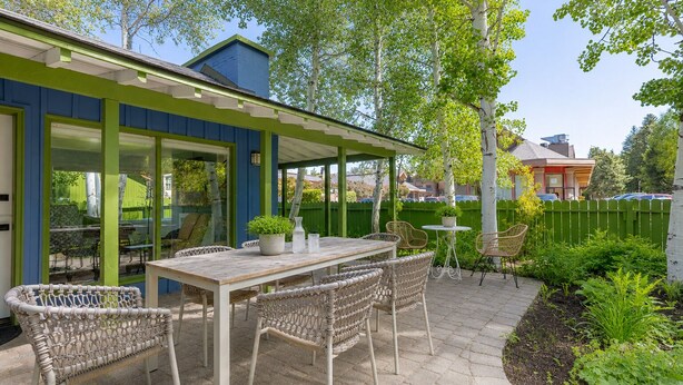 Un patio con una mesa y sillas, cercado con una valla verde, y un edificio con paredes exteriores azules y verdes.