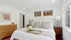 Un dormitorio ordenado con cama, cómoda, lámparas de noche y obras de arte en las paredes.