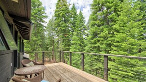 Un terrazzo in legno con mobili in vimini e vista su alberi verdi e fitti.