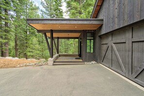A modern building with a covered porch, large garage doors, and a forested backdrop. - Sierra Sanctuary by Tahoe Getaways - Beautiful 5BR w/ Hot Tub & Private Outdoor Area (Truckee)