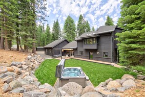 A modern two-story house with a hot tub in the front yard, surrounded by a rock garden and a well-maintained lawn. - Sierra Sanctuary by Tahoe Getaways - Beautiful 5BR w/ Hot Tub & Private Outdoor Area (Truckee)