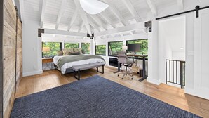 Una camera da letto con un letto, una scrivania, un computer, ampie finestre e un soffitto alto.