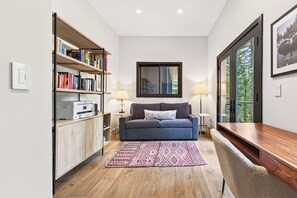 Ein modernes Wohnzimmer mit einer Couch, einem Bücherregal, einem Schreibtisch und einem großen Fenster.