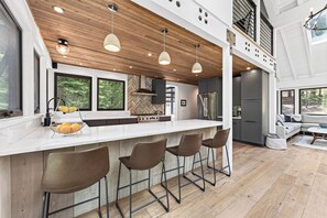 Eine moderne Küche mit Holzboden, weißen Arbeitsplatten und Barhocker.