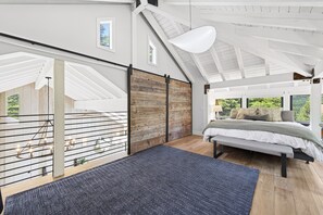 A bedroom with a bed, a large window, a wooden wall, and a hanging light fixture. - Sierra Sanctuary by Tahoe Getaways - Beautiful 5BR w/ Hot Tub & Private Outdoor Area (Truckee)