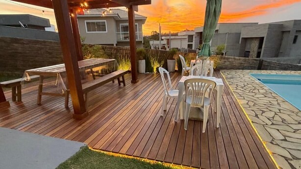 A wooden deck with outdoor furniture, a pool, and a sunset view. - Pousada Requinte da Serra  (Miguel Pereira)