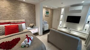 A modern bedroom with a bed, a sofa, a TV, and a microwave. - Pousada Requinte da Serra  (Miguel Pereira)