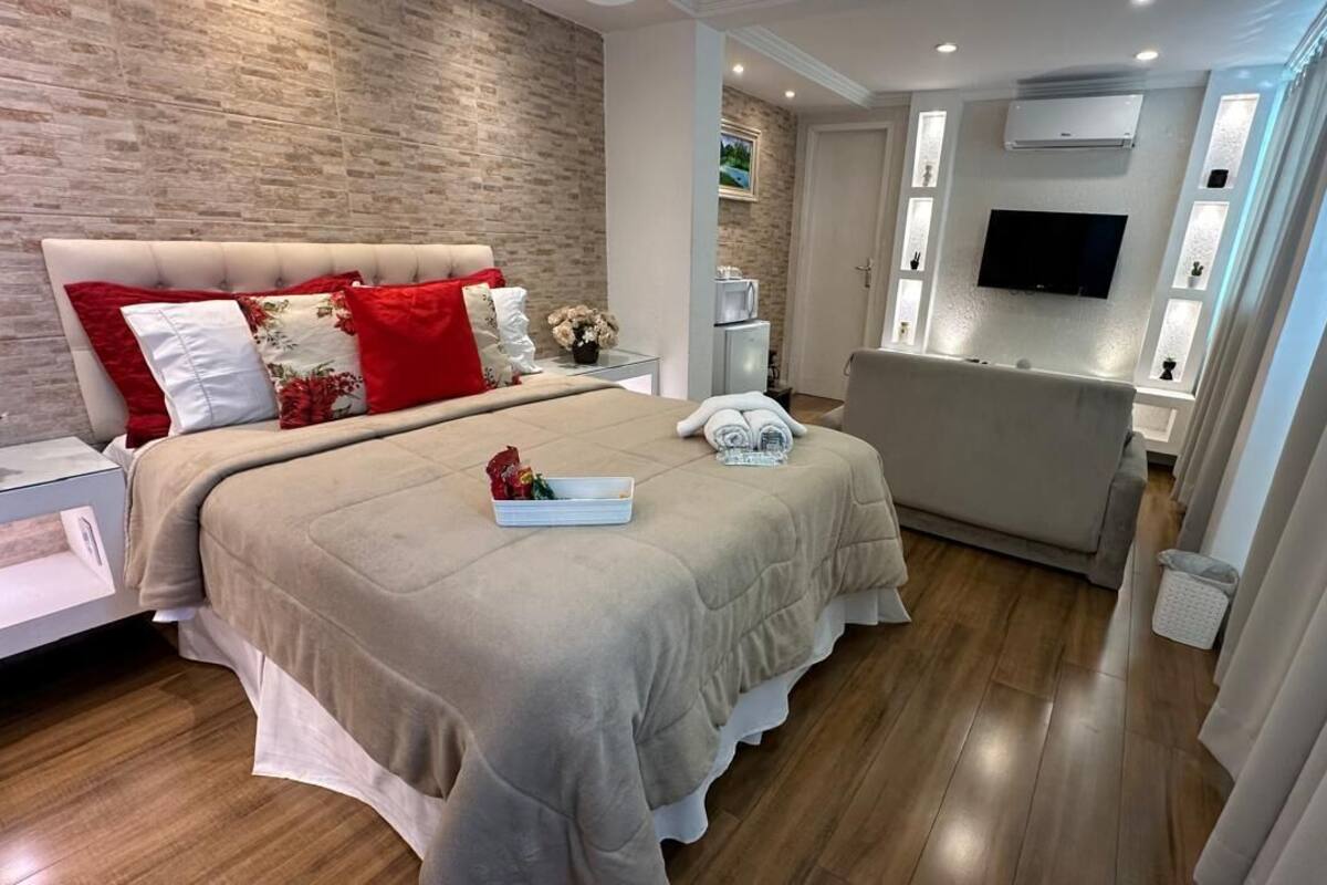 A modern hotel room with a large bed, a sofa, a TV, and a bathroom with a shower and toilet.