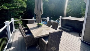 Een terras met een tafel en stoelen, een overdekte parasol en uitzicht op bomen.