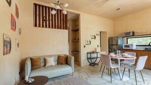 A modern living room with a sofa, dining table, and chairs, a kitchen area with appliances, and a staircase. - Depto. Eek’ · 1 Hab · 1 Baño · Terraza Privada (Merida)
