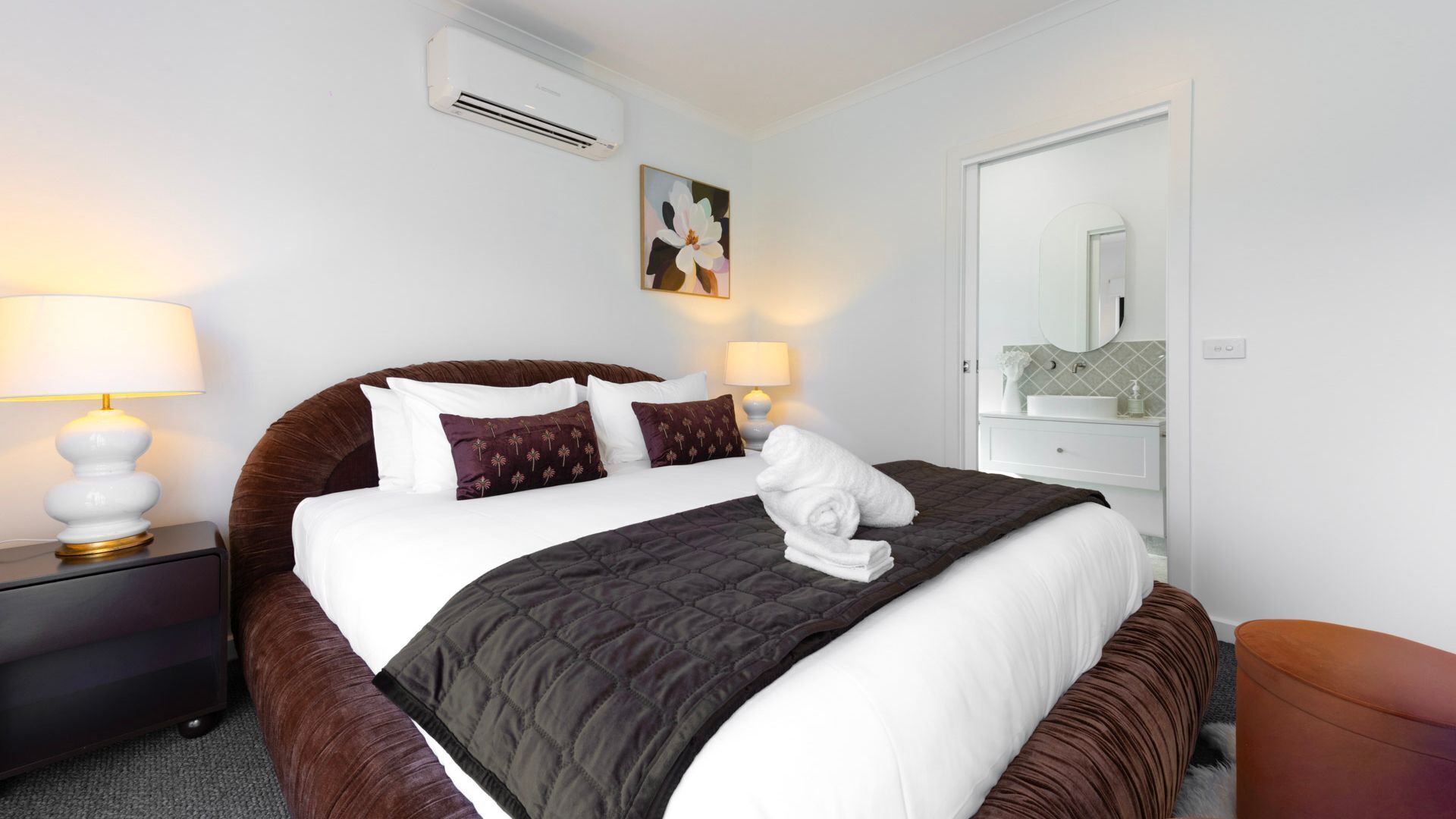 Une chambre d’hôtel avec un grand lit, deux lampes de chevet, un appareil de climatisation, un tableau, un miroir et une salle de bain équipée d’un lavabo et d’un miroir.