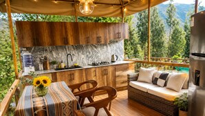 A cozy outdoor kitchen with wooden cabinets and a marble backsplash, overlooking a lush green landscape.