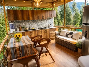 A cozy outdoor kitchen with wooden cabinets and a marble backsplash, overlooking a lush green landscape.
