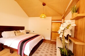 Un dormitorio con techo de madera, cama con ropa de cama blanca, lámpara colgante y estante en la pared con plantas.