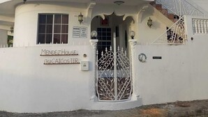 Un edificio blanco con varias ventanas, una entrada protegida por un portón y un cartel que dice 'MENDEZ HOUSE'.
