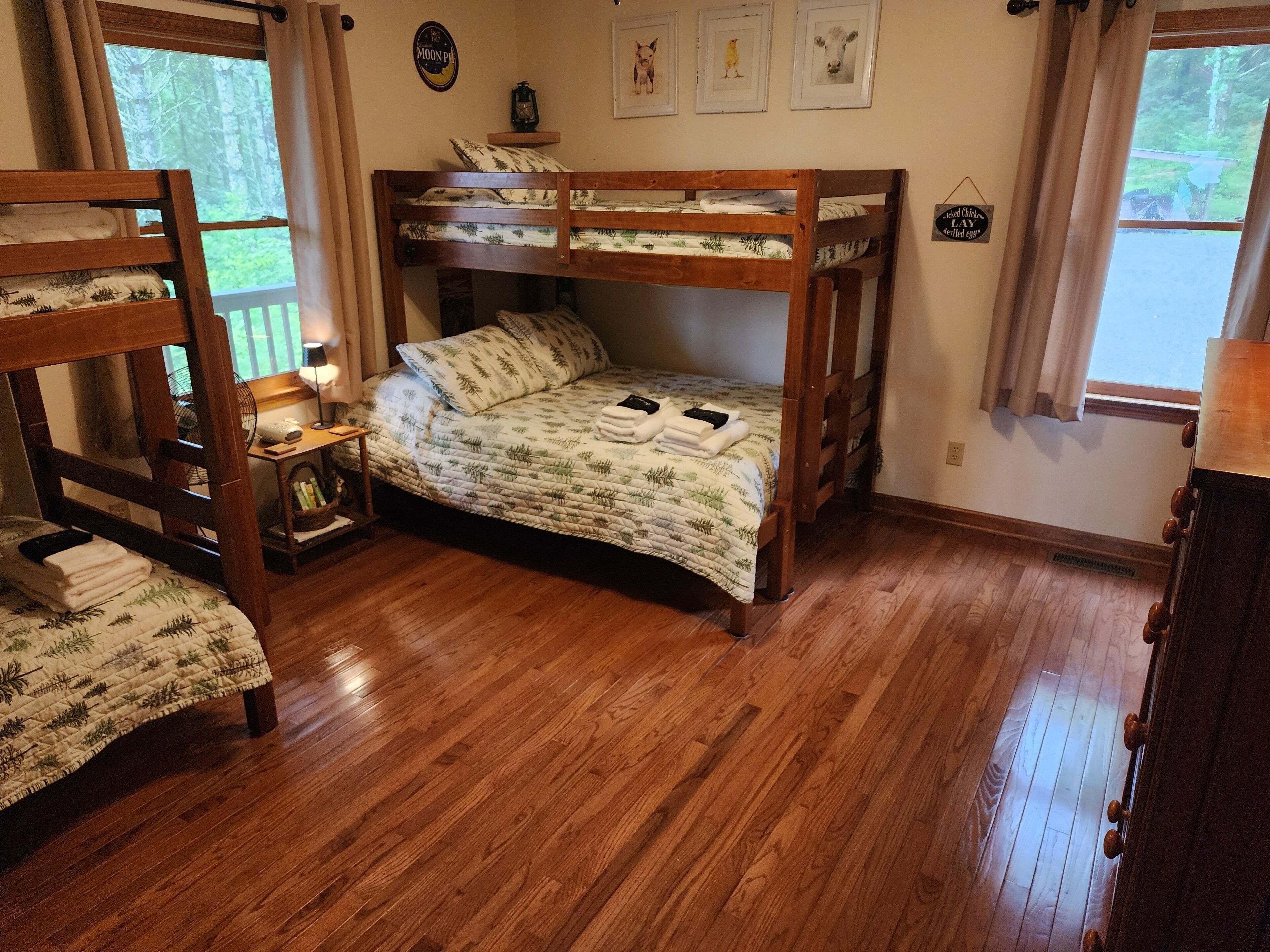 A bunk bed room with a wooden floor, a bedside table with a lamp, and framed pictures on the wall.