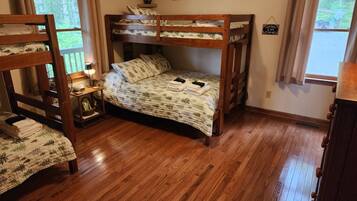 A bunk bed room with a wooden floor, a bedside table with a lamp, and framed pictures on the wall.