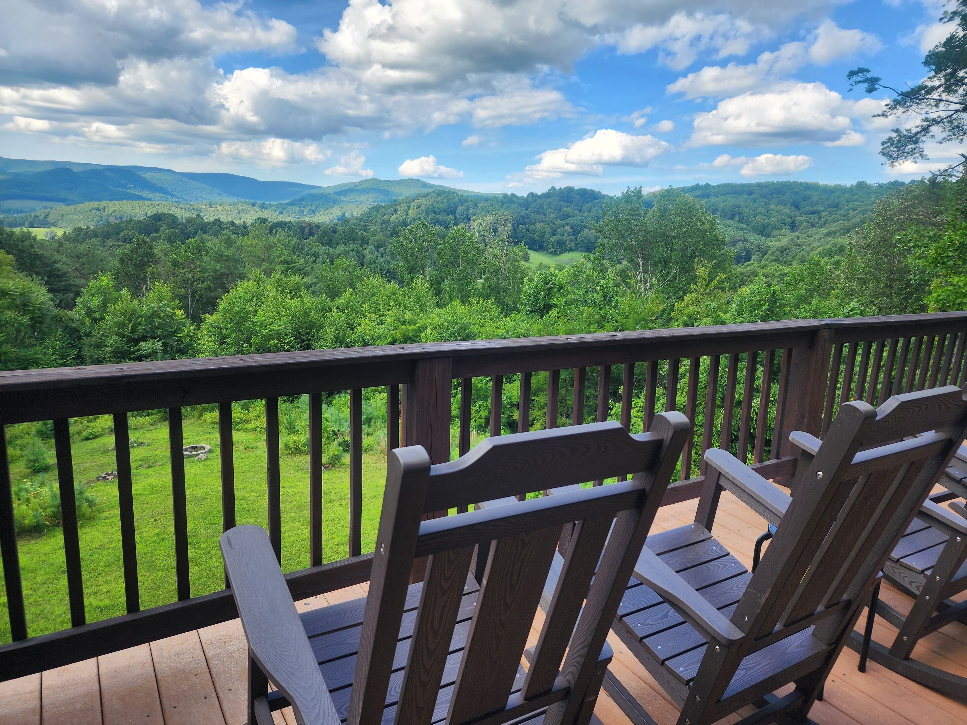 A deck with wooden chairs overlooking a lush green landscape with distant hills.