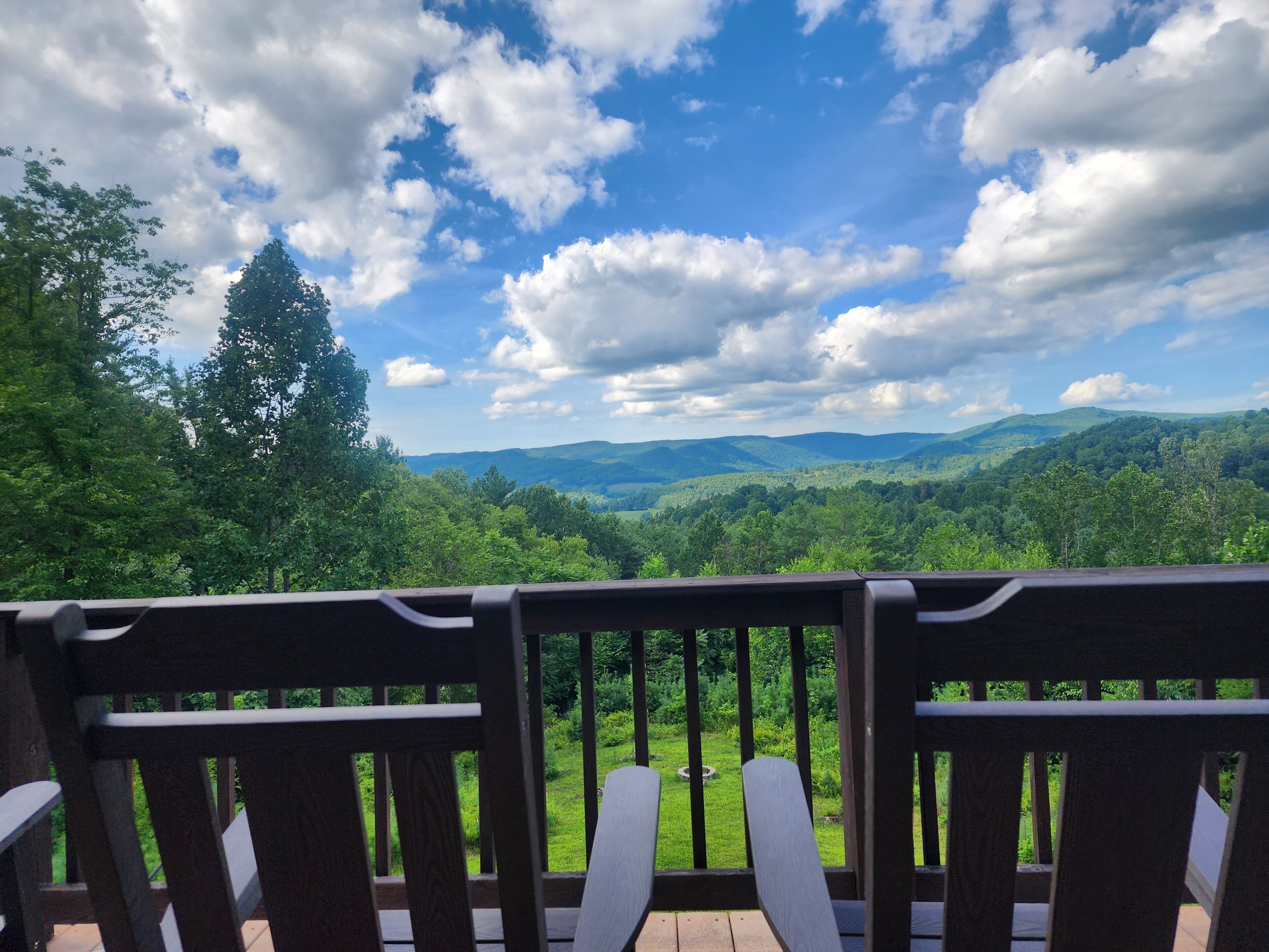 Une terrasse en bois offrant une vue sur un paysage boisé et des collines lointaines.
