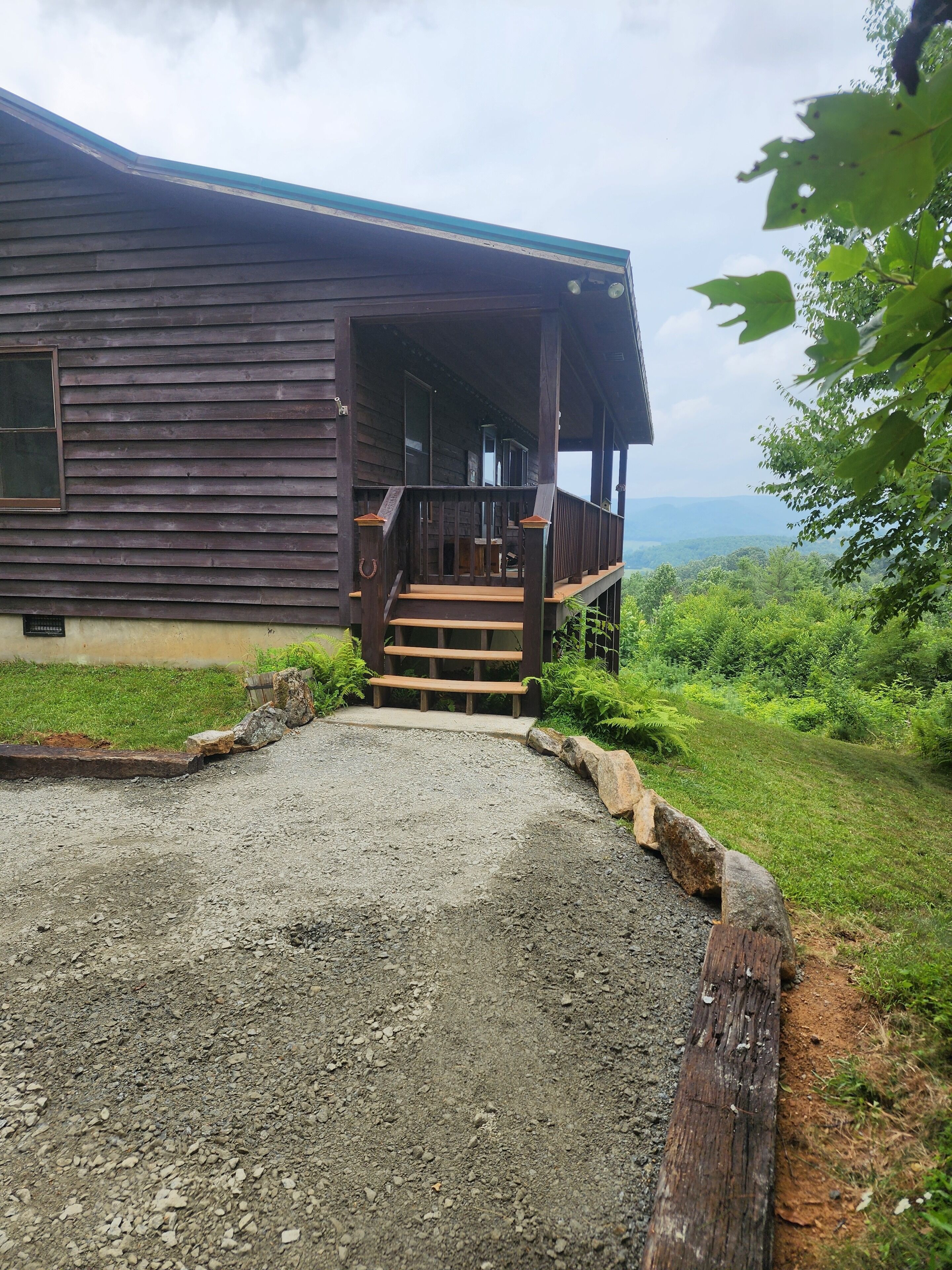 A wooden cabin with a porch and steps leading to a gravel driveway.