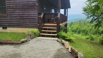 A wooden cabin with a porch and steps leading to a gravel driveway.