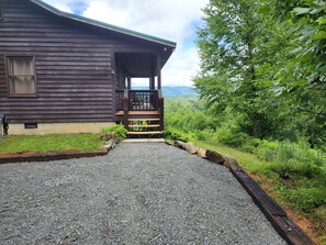 A wooden cabin with a gravel driveway leading to a porch with steps.
