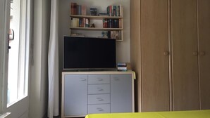 A room with a TV on a cabinet, a bookshelf, a wardrobe, and a window with curtains. - Amici 13 Appartement/Fewo 2-Bettwohnung by Interhome (Saas-Fee)