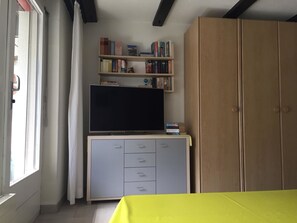 Ein Zimmer mit Fernseher auf einem Schrank, einem Bücherregal, einem Kleiderschrank und einem Fenster mit Vorhängen.