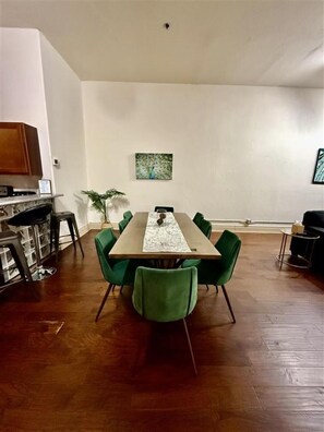 Un coin repas avec une longue table, des chaises vertes, une plante en pot et un tableau accroché au mur.