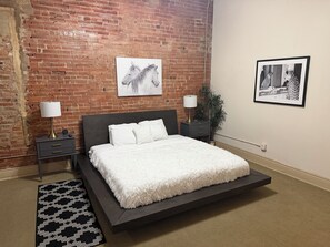 Une chambre moderne avec un mur en briques, un grand lit, deux tables de chevet avec des lampes et des œuvres d’art.