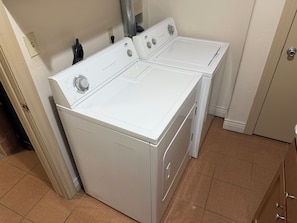A laundry room with two white front-loading washers and dryers, a tiled floor, and a door to the right. - The Safari Unit 2 Downtown Loft Sleeps 4 (Oklahoma City)