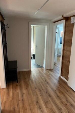 Een gang met houten vloer, een bankje en een deur naar een andere kamer.