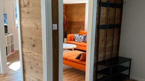 Ein Innenraum mit Holzboden, einem Bett mit orangefarbener Bettwäsche und einer schwarzen Metallbank.