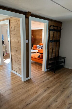 Een interieur met een houten vloer, een bed met oranje beddengoed en een zwarte metalen bank.