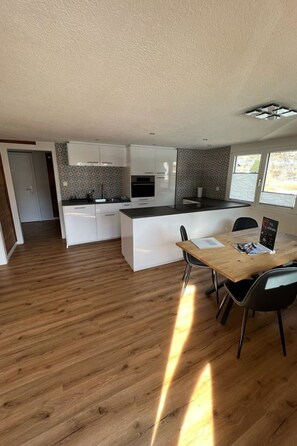 Een moderne keuken met witte kasten, een houten eettafel en uitzicht op het omliggende landschap.