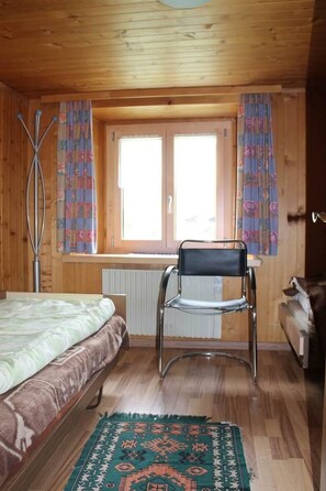 Ein Zimmer mit einem Bett, einem Sessel, einer Heizung und einem fenster mit Vorhängen.