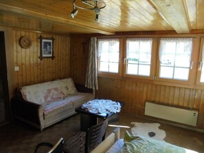 Ein Holzblockhaus-Innenraum mit einer Couch, einem Tisch mit Papieren, einer Heizung und einem Fenster mit Blick nach draußen.