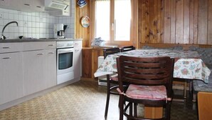 Een keuken met witte kastjes, een fornuis, een spoelbak en een eethoek met een tafel en stoelen.
