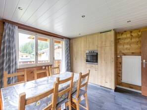 A wooden interior with a dining table, chairs, a kitchen area with a stove, and a view of houses outside. - Weideli Appartement/Fewo 6-Bettwohnung Nr. 20 by Interhome (Saas-Balen)