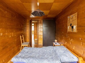 A wooden cabin room with a bed, a chair, a table with a lamp, and a door leading to another room. - Weideli Appartement/Fewo 6-Bettwohnung Nr. 20 by Interhome (Saas-Balen)