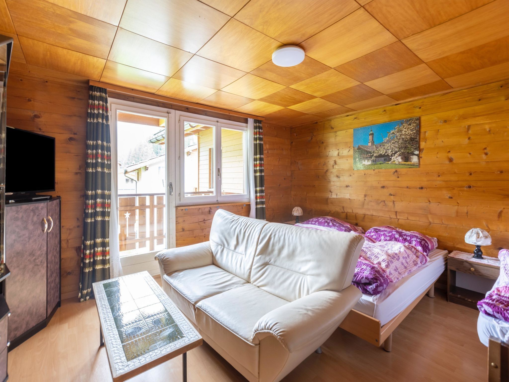 Une cabane en bois avec un canapé, un lit, une télévision et un tableau accroché au mur.