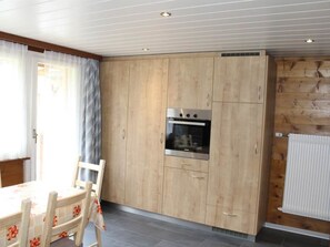 A kitchen with wooden cabinets, a built-in oven, and a dining area with a table and chairs. - Weideli Appartement/Fewo 6-Bettwohnung Nr. 20 by Interhome (Saas-Balen)